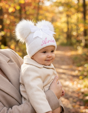 Load image into Gallery viewer, Baby girl wearing the Aria hat held in a parent’s arms in woodland
