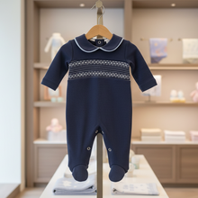 Load image into Gallery viewer, Navy smocked babygrow on wooden hanger in boutique